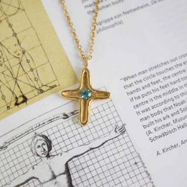 Discover the elegance of the Maria’s Cross necklace with light blue stone, a piece that blends timeless symbolism with artisanal craftsmanship. Handmade from high-quality brass and plated with radiant 24k gold, this cross pendant carries a soft light blue gemstone at its center, symbolizing serenity, hope, and inner peace.Ανακαλύψτε την κομψότητα του κολιέ Maria’s Cross με γαλάζια πέτρα, ένα κόσμημα που συνδυάζει διαχρονικό συμβολισμό με χειροποίητη τέχνη. Κατασκευασμένο στο χέρι από ορείχαλκο υψηλής ποιότητας και επιχρυσωμένο με 24 καράτια χρυσό, το μενταγιόν σε σχήμα σταυρού φιλοξενεί μια γαλάζια πέτρα στο κέντρο του, που συμβολίζει τη γαλήνη, την ελπίδα και την εσωτερική αρμονία.