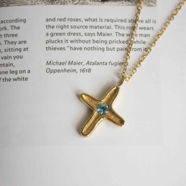 Discover the elegance of the Maria’s Cross necklace with light blue stone, a piece that blends timeless symbolism with artisanal craftsmanship. Handmade from high-quality brass and plated with radiant 24k gold, this cross pendant carries a soft light blue gemstone at its center, symbolizing serenity, hope, and inner peace.Ανακαλύψτε την κομψότητα του κολιέ Maria’s Cross με γαλάζια πέτρα, ένα κόσμημα που συνδυάζει διαχρονικό συμβολισμό με χειροποίητη τέχνη. Κατασκευασμένο στο χέρι από ορείχαλκο υψηλής ποιότητας και επιχρυσωμένο με 24 καράτια χρυσό, το μενταγιόν σε σχήμα σταυρού φιλοξενεί μια γαλάζια πέτρα στο κέντρο του, που συμβολίζει τη γαλήνη, την ελπίδα και την εσωτερική αρμονία.
