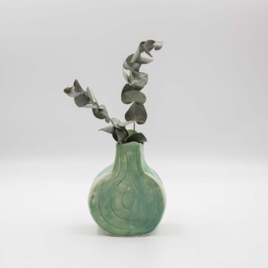 handmade ceramic vase with a glossy glaze displayed on a wooden surface. The vase showcases exquisite craftsmanship, with intricate details and a smooth finish. Its glazed surface adds a subtle sheen, enhancing the vase's elegance and making it a beautiful centerpiece for any room.