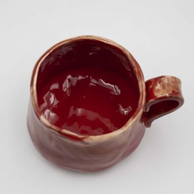 handmade ceramic mugs with a unique glazing technique. The mugs feature a rich, deep red color with subtle variations and textures, creating a visually captivating effect. The special glazing adds depth and dimension to the mugs' surface, making them both functional and aesthetically pleasing.