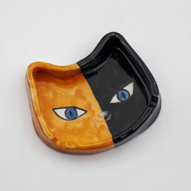 A handmade ceramic calico cat ashtray, featuring a tri-color cat design with orange, black, and white patches, perfect for holding ash and cigarettes. Ένα χειροποίητο κεραμικό τασάκι γάτας κάλικο, με σχέδιο τριχρωμίας γάτας με πορτοκαλί, μαύρες και λευκές περιοχές, ιδανικό για την αποθήκευση στάχτης και τσιγάρων.