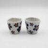 Handmade ceramic cups featuring delicate floral designs, showcasing intricate craftsmanship and artistic detail. Χειροποίητα κεραμικά φλιτζάνια με λουλούδια, παρουσιάζοντας λεπτομερή τεχνική και καλλιτεχνική λεπτομέρεια.