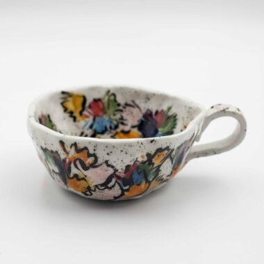 A close-up image of a ceramic handmade floral mug, showcasing intricate floral designs and vibrant colors on a smooth surface. Κοντινή εικόνα μιας κεραμικής χειροποίητης κούπας με λουλουδένια μοτίβα, επιδεικνύοντας λεπτομερείς σχεδιασμούς λουλουδιών και ζωηρά χρώματα σε λεία επιφάνεια.