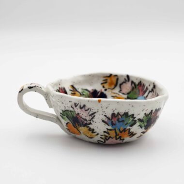 A close-up image of a ceramic handmade floral mug, showcasing intricate floral designs and vibrant colors on a smooth surface. Κοντινή εικόνα μιας κεραμικής χειροποίητης κούπας με λουλουδένια μοτίβα, επιδεικνύοντας λεπτομερείς σχεδιασμούς λουλουδιών και ζωηρά χρώματα σε λεία επιφάνεια.