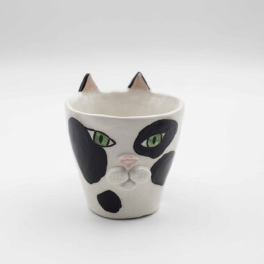 Close-up of a ceramic handmade cat tuxedo mug, featuring a black and white tuxedo cat design on a white mug. Κοντινή λήψη μιας χειροποίητης κεραμικής κούπας με μοτίβο γάτας με μαύρο και λευκό σχέδιο σε ένα λευκό κύπελλο.