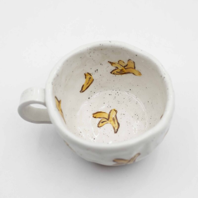 Close-up of a ceramic handmade mug with banana motifs . Κοντινή λήψη μιας χειροποίητης κεραμικής κούπας με μοτίβα μπανανών.