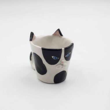 Close-up of a ceramic handmade cat tuxedo cup , featuring a black and white tuxedo cat design on a white mug. Κοντινή λήψη ενός χειροποίητου κεραμικού φλιτζανιού με μοτίβο γάτας με μαύρο και λευκό σχέδιο σε ένα λευκό κύπελλο.