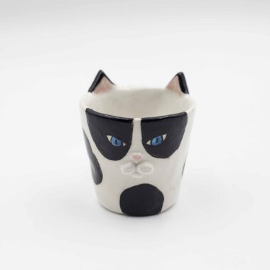 Close-up of a ceramic handmade cat tuxedo cup , featuring a black and white tuxedo cat design on a white mug. Κοντινή λήψη ενός χειροποίητου κεραμικού φλιτζανιού με μοτίβο γάτας με μαύρο και λευκό σχέδιο σε ένα λευκό κύπελλο.