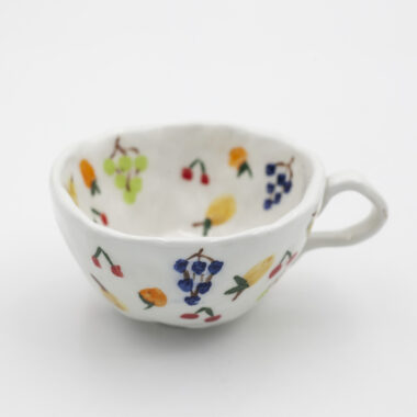 Μια μοναδική χειροποίητη κεραμική κούπα με διάφορα φρούτα ζωγραφισμένα πάνω της αναδεικνύοντας την ξεχωριστή της ομορφιά. A unique handmade ceramic mug with various fruits on it, showcasing its distinctive beauty.