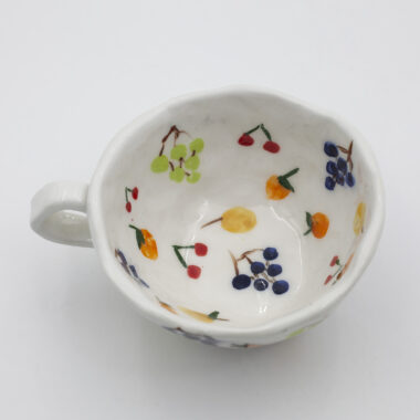 Μια μοναδική χειροποίητη κεραμική κούπα με διάφορα φρούτα ζωγραφισμένα πάνω της αναδεικνύοντας την ξεχωριστή της ομορφιά. A unique handmade ceramic mug with various fruits on it, showcasing its distinctive beauty.
