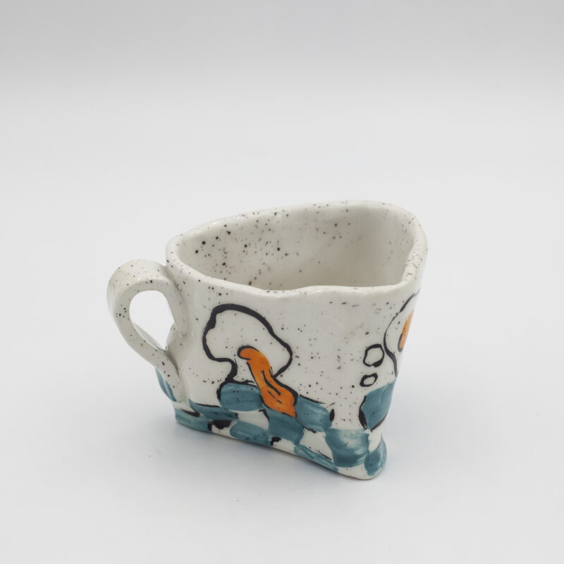 Μια χειροποίητη κεραμική κούπα με αυγά και γαλάζιο πάτωμα σκακιέρα που δημιουργεί μια σουρεαλιστική αίσθηση. English: A handmade ceramic mug adorned with eggs, creating a surrealistic sensation.