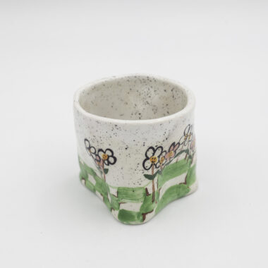 Μια χειροποίητη κεραμική κούπα με σουρεαλιστικά κινούμενα λουλούδια με πρόσωπα. A handmade ceramic mug with surreal cartoon flowers with faces on them.