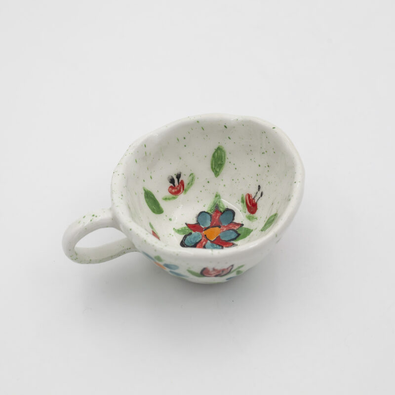 Μια χειροποίητη κεραμική κούπα με λουλούδια. A handmade ceramic cup with flowers.