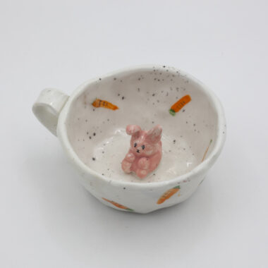 Μια χειροποίητη κεραμική κούπα με σχέδια καρότων πάνω της και μέσα σε αυτήν ένα 3D κουνελάκι. A handmade ceramic mug with carrot drawings on it, and inside it, a 3D bunny.