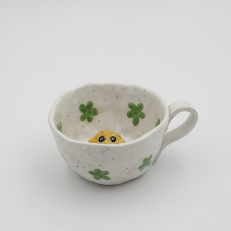 Μια χειροποίητη κεραμική κούπα με σχέδια λουλουδιών πάνω της και μέσα σε αυτήν ένα 3D κοτοπουλάκι. A handmade ceramic mug with flowers drawings on it, and inside it, a 3D chicken.