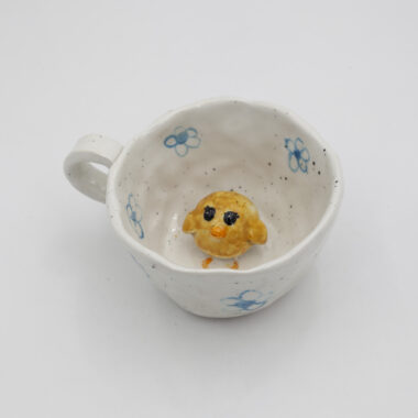 Μια χειροποίητη κεραμική κούπα με σχέδια λουλουδιών πάνω της και μέσα σε αυτήν ένα 3D κοτοπουλάκι. A handmade ceramic mug with flowers drawings on it, and inside it, a 3D chicken.