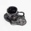 Black ceramic mug with curved floral design, paired with a matching black saucer. Perfect for enjoying your favorite beverage in style. keywords: black mug, floral mug, curved flowers, mug with saucer, ceramic mug Μαύρο φλιτζάνι από κεραμικό με ανάγλυφο floral σχέδιο, μαζί με μαύρο πιατάκι. Ιδανικό για να απολαύσετε το αγαπημένο σας ρόφημα με στυλ. keywords: μαύρο φλιτζάνι, floral φλιτζάνι, ανάγλυφα λουλούδια, φλιτζάνι με πιατάκι, κεραμικό φλιτζάνι