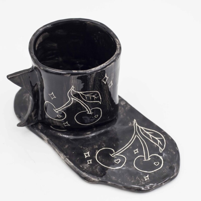 Black ceramic mug with curved floral design, paired with a matching black saucer. Perfect for enjoying your favorite beverage in style. keywords: black mug, floral mug, curved flowers, mug with saucer, ceramic mug Μαύρο φλιτζάνι από κεραμικό με ανάγλυφο floral σχέδιο, μαζί με μαύρο πιατάκι. Ιδανικό για να απολαύσετε το αγαπημένο σας ρόφημα με στυλ. keywords: μαύρο φλιτζάνι, floral φλιτζάνι, ανάγλυφα λουλούδια, φλιτζάνι με πιατάκι, κεραμικό φλιτζάνι