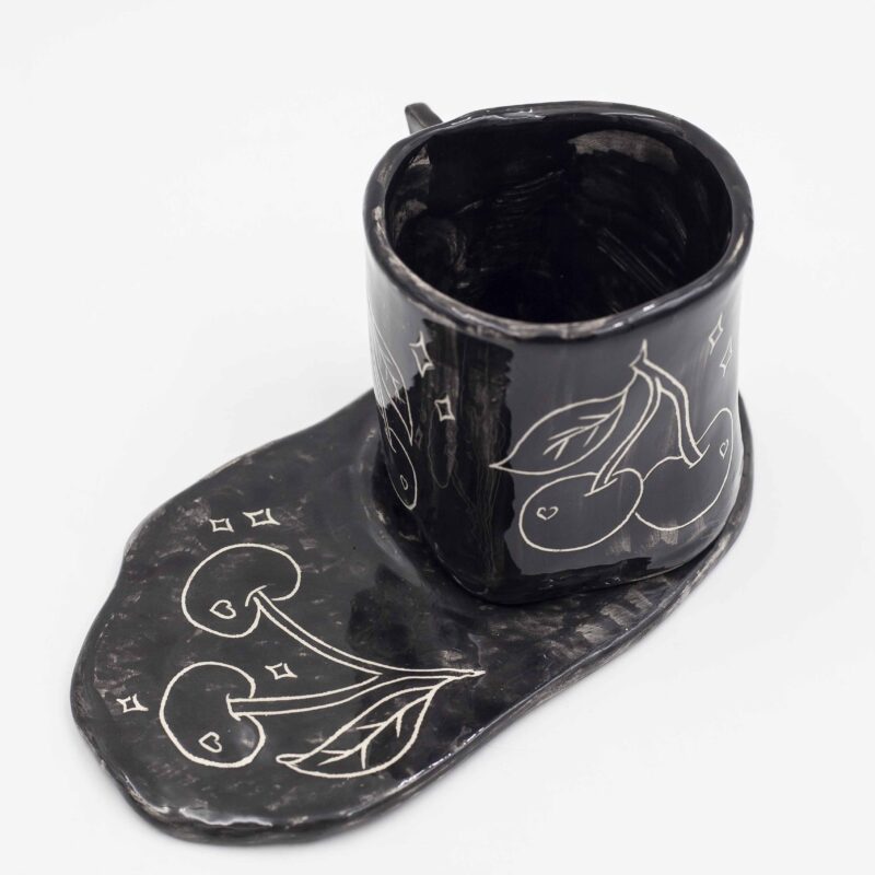 Black ceramic mug with curved floral design, paired with a matching black saucer. Perfect for enjoying your favorite beverage in style. keywords: black mug, floral mug, curved flowers, mug with saucer, ceramic mug Μαύρο φλιτζάνι από κεραμικό με ανάγλυφο floral σχέδιο, μαζί με μαύρο πιατάκι. Ιδανικό για να απολαύσετε το αγαπημένο σας ρόφημα με στυλ. keywords: μαύρο φλιτζάνι, floral φλιτζάνι, ανάγλυφα λουλούδια, φλιτζάνι με πιατάκι, κεραμικό φλιτζάνι