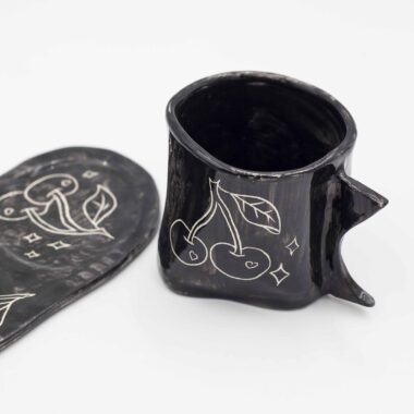 Black ceramic mug with curved floral design, paired with a matching black saucer. Perfect for enjoying your favorite beverage in style. keywords: black mug, floral mug, curved flowers, mug with saucer, ceramic mug Μαύρο φλιτζάνι από κεραμικό με ανάγλυφο floral σχέδιο, μαζί με μαύρο πιατάκι. Ιδανικό για να απολαύσετε το αγαπημένο σας ρόφημα με στυλ. keywords: μαύρο φλιτζάνι, floral φλιτζάνι, ανάγλυφα λουλούδια, φλιτζάνι με πιατάκι, κεραμικό φλιτζάνι