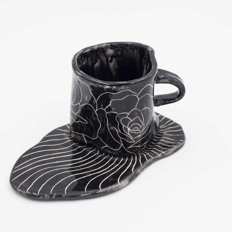 Black ceramic mug with curved floral design, paired with a matching black saucer. Perfect for enjoying your favorite beverage in style. keywords: black mug, floral mug, curved flowers, mug with saucer, ceramic mug Μαύρο φλιτζάνι από κεραμικό με ανάγλυφο floral σχέδιο, μαζί με μαύρο πιατάκι. Ιδανικό για να απολαύσετε το αγαπημένο σας ρόφημα με στυλ. keywords: μαύρο φλιτζάνι, floral φλιτζάνι, ανάγλυφα λουλούδια, φλιτζάνι με πιατάκι, κεραμικό φλιτζάνι