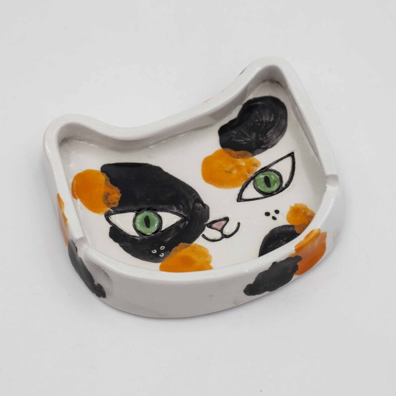 A handmade ceramic calico cat ashtray, featuring a black and white cat design with intricate detailing, perfect for holding ash and cigarettes. Ένα χειροποίητο κεραμικό τασάκι γάτας με σχέδιο μαύρης και λευκής γάτας με λεπτομερείς λεπτομέρειες, ιδανικό για την αποθήκευση στάχτης και τσιγάρων.