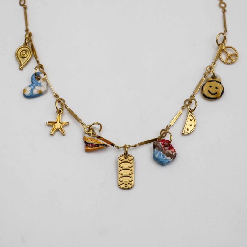 Handmade ceramic charm necklace featuring intricate designs, complemented by golden metallic brass charms and a sturdy steel chain. This unique and elegant accessory adds a touch of artisan craftsmanship and sophistication to any outfit, perfect for both casual and formal occasions. Χειροποίητο κολιέ με κεραμικά γούρια που διαθέτουν περίτεχνα σχέδια, συμπληρωμένα με χρυσά μεταλλικά γούρια από μπρούντζο και ανθεκτική αλυσίδα από ατσάλι. Αυτό το μοναδικό και κομψό αξεσουάρ προσθέτει μια πινελιά καλλιτεχνικής δεξιοτεχνίας και εκλέπτυνσης σε κάθε ντύσιμο, ιδανικό για κάθε περίσταση, είτε επίσημη είτε καθημερινή.