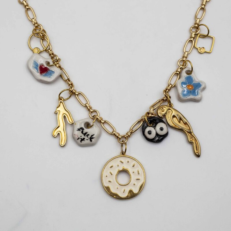 Handmade ceramic charm necklace featuring intricate designs, complemented by golden metallic brass charms and a sturdy steel chain. This unique and elegant accessory adds a touch of artisan craftsmanship and sophistication to any outfit, perfect for both casual and formal occasions. Χειροποίητο κολιέ με κεραμικά γούρια που διαθέτουν περίτεχνα σχέδια, συμπληρωμένα με χρυσά μεταλλικά γούρια από μπρούντζο και ανθεκτική αλυσίδα από ατσάλι. Αυτό το μοναδικό και κομψό αξεσουάρ προσθέτει μια πινελιά καλλιτεχνικής δεξιοτεχνίας και εκλέπτυνσης σε κάθε ντύσιμο, ιδανικό για κάθε περίσταση, είτε επίσημη είτε καθημερινή.