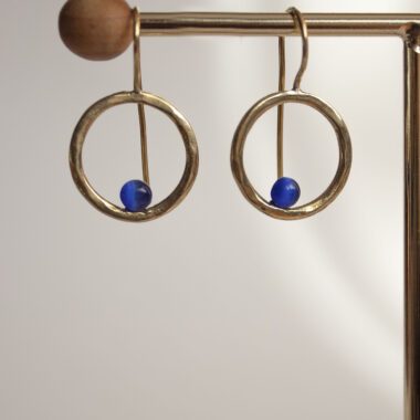 Handmade brass Phaidra circle earrings featuring beautiful blue cat eye stones, crafted by Sunny Designs. These elegant and stylish earrings are perfect for adding a touch of sophistication to any outfit and make a wonderful gift for women. Phaidra earrings, circle earrings, blue cat eye earrings, handmade brass jewelry, Sunny Designs earrings, unique gift, stylish earrings, women’s jewelry, artisan earrings, elegant earrings Χειροποίητα σκουλαρίκια Phaidra σε σχήμα κύκλου από μπρούντζο με όμορφες μπλε πέτρες ματιού της γάτας, φτιαγμένα από τη Sunny Designs. Αυτά τα κομψά και στιλάτα σκουλαρίκια είναι ιδανικά για να προσθέσουν μια αίσθηση κομψότητας σε κάθε ντύσιμο και αποτελούν μια υπέροχη επιλογή δώρου για γυναίκες. σκουλαρίκια Phaidra, κυκλικά σκουλαρίκια, σκουλαρίκια με μπλε μάτι γάτας, χειροποίητο κόσμημα από μπρούντζο, σκουλαρίκια Sunny Designs, μοναδικό δώρο, κομψά σκουλαρίκια, γυναικείο κόσμημα, κοσμήματα τέχνης, κομψά σκουλαρίκια