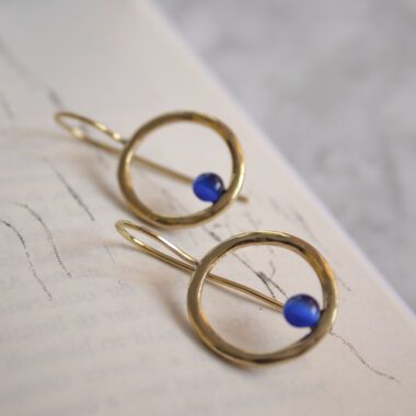 Handmade brass Phaidra circle earrings featuring beautiful blue cat eye stones, crafted by Sunny Designs. These elegant and stylish earrings are perfect for adding a touch of sophistication to any outfit and make a wonderful gift for women. Phaidra earrings, circle earrings, blue cat eye earrings, handmade brass jewelry, Sunny Designs earrings, unique gift, stylish earrings, women’s jewelry, artisan earrings, elegant earrings Χειροποίητα σκουλαρίκια Phaidra σε σχήμα κύκλου από μπρούντζο με όμορφες μπλε πέτρες ματιού της γάτας, φτιαγμένα από τη Sunny Designs. Αυτά τα κομψά και στιλάτα σκουλαρίκια είναι ιδανικά για να προσθέσουν μια αίσθηση κομψότητας σε κάθε ντύσιμο και αποτελούν μια υπέροχη επιλογή δώρου για γυναίκες. σκουλαρίκια Phaidra, κυκλικά σκουλαρίκια, σκουλαρίκια με μπλε μάτι γάτας, χειροποίητο κόσμημα από μπρούντζο, σκουλαρίκια Sunny Designs, μοναδικό δώρο, κομψά σκουλαρίκια, γυναικείο κόσμημα, κοσμήματα τέχνης, κομψά σκουλαρίκια