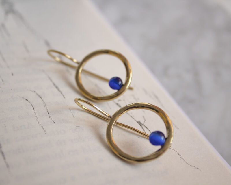 Handmade brass Phaidra circle earrings featuring beautiful blue cat eye stones, crafted by Sunny Designs. These elegant and stylish earrings are perfect for adding a touch of sophistication to any outfit and make a wonderful gift for women. Phaidra earrings, circle earrings, blue cat eye earrings, handmade brass jewelry, Sunny Designs earrings, unique gift, stylish earrings, women’s jewelry, artisan earrings, elegant earrings Χειροποίητα σκουλαρίκια Phaidra σε σχήμα κύκλου από μπρούντζο με όμορφες μπλε πέτρες ματιού της γάτας, φτιαγμένα από τη Sunny Designs. Αυτά τα κομψά και στιλάτα σκουλαρίκια είναι ιδανικά για να προσθέσουν μια αίσθηση κομψότητας σε κάθε ντύσιμο και αποτελούν μια υπέροχη επιλογή δώρου για γυναίκες. σκουλαρίκια Phaidra, κυκλικά σκουλαρίκια, σκουλαρίκια με μπλε μάτι γάτας, χειροποίητο κόσμημα από μπρούντζο, σκουλαρίκια Sunny Designs, μοναδικό δώρο, κομψά σκουλαρίκια, γυναικείο κόσμημα, κοσμήματα τέχνης, κομψά σκουλαρίκια