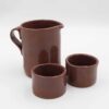 Handmade ceramic jug with two matching cups, crafted from rich red clay and finished with a transparent glaze that beautifully reveals the natural earthy tones. This artisanal set combines functionality with elegance, making it perfect for serving beverages with a rustic, handmade charm. Ideal for adding a touch of natural beauty to your kitchen or table decor. Χειροποίητη κεραμική κανάτα με δύο αντίστοιχες κούπες, κατασκευασμένες από κόκκινο πηλό και καλυμμένες με διάφανο γυαλί που αναδεικνύει τους φυσικούς γήινους τόνους. Αυτό το καλλιτεχνικό σετ συνδυάζει λειτουργικότητα με κομψότητα, ιδανικό για το σερβίρισμα ροφημάτων με μια ρουστίκ, χειροποίητη αίσθηση. Ιδανικό για να προσθέσετε μια φυσική ομορφιά στην κουζίνα ή το τραπέζι σας.