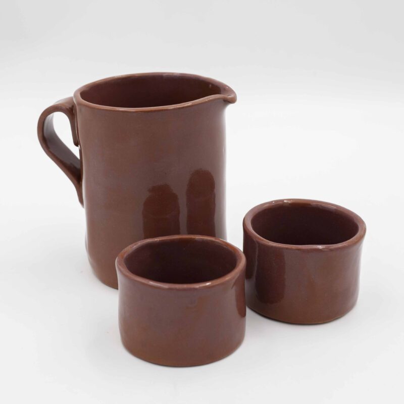 Handmade ceramic jug with two matching cups, crafted from rich red clay and finished with a transparent glaze that beautifully reveals the natural earthy tones. This artisanal set combines functionality with elegance, making it perfect for serving beverages with a rustic, handmade charm. Ideal for adding a touch of natural beauty to your kitchen or table decor. Χειροποίητη κεραμική κανάτα με δύο αντίστοιχες κούπες, κατασκευασμένες από κόκκινο πηλό και καλυμμένες με διάφανο γυαλί που αναδεικνύει τους φυσικούς γήινους τόνους. Αυτό το καλλιτεχνικό σετ συνδυάζει λειτουργικότητα με κομψότητα, ιδανικό για το σερβίρισμα ροφημάτων με μια ρουστίκ, χειροποίητη αίσθηση. Ιδανικό για να προσθέσετε μια φυσική ομορφιά στην κουζίνα ή το τραπέζι σας.