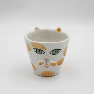 Handmade ceramic mug with a cat face design, available in calico, tuxedo, white, and orange cat variations. Perfect for cat lovers looking to add a cute, personalized touch to their drinkware collection." Greek: "Χειροποίητη κεραμική κούπα με σχέδιο προσώπου γάτας, διαθέσιμη σε εκδόσεις τρίχρωμης, δίχρωμης, λευκής και πορτοκαλί γάτας. Ιδανική για φιλόζωους που θέλουν να προσθέσουν μια χαριτωμένη, προσωπική πινελιά στη συλλογή τους από κούπες.