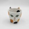 Handmade ceramic mug with a cat face design, available in calico, tuxedo, white, and orange cat variations. Perfect for cat lovers looking to add a cute, personalized touch to their drinkware collection." Greek: "Χειροποίητη κεραμική κούπα με σχέδιο προσώπου γάτας, διαθέσιμη σε εκδόσεις τρίχρωμης, δίχρωμης, λευκής και πορτοκαλί γάτας. Ιδανική για φιλόζωους που θέλουν να προσθέσουν μια χαριτωμένη, προσωπική πινελιά στη συλλογή τους από κούπες.