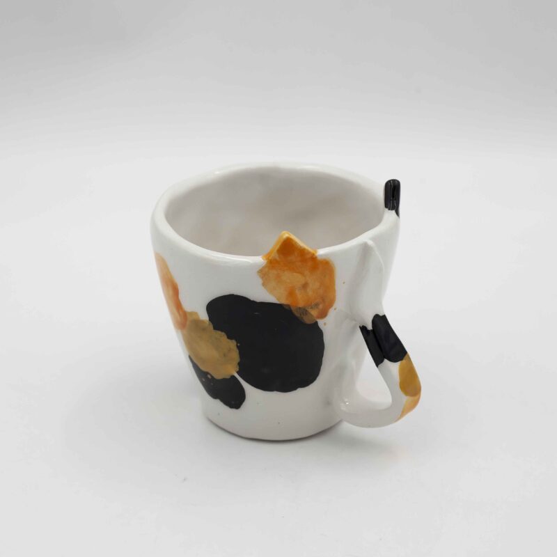 Handmade ceramic mug with a cat face design, available in calico, tuxedo, white, and orange cat variations. Perfect for cat lovers looking to add a cute, personalized touch to their drinkware collection." Greek: "Χειροποίητη κεραμική κούπα με σχέδιο προσώπου γάτας, διαθέσιμη σε εκδόσεις τρίχρωμης, δίχρωμης, λευκής και πορτοκαλί γάτας. Ιδανική για φιλόζωους που θέλουν να προσθέσουν μια χαριτωμένη, προσωπική πινελιά στη συλλογή τους από κούπες.