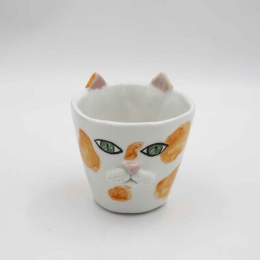 Handmade ceramic mug with a cat face design, available in calico, tuxedo, white, and orange cat variations. Perfect for cat lovers looking to add a cute, personalized touch to their drinkware collection." Greek: "Χειροποίητη κεραμική κούπα με σχέδιο προσώπου γάτας, διαθέσιμη σε εκδόσεις τρίχρωμης, δίχρωμης, λευκής και πορτοκαλί γάτας. Ιδανική για φιλόζωους που θέλουν να προσθέσουν μια χαριτωμένη, προσωπική πινελιά στη συλλογή τους από κούπες.