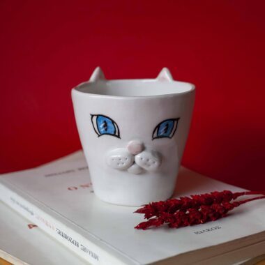 Handmade ceramic mug with a cat face design, available in calico, tuxedo, white, and orange cat variations. Perfect for cat lovers looking to add a cute, personalized touch to their drinkware collection.