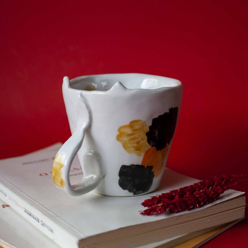 Handmade ceramic mug with a cat face design, available in calico, tuxedo, white, and orange cat variations. Perfect for cat lovers looking to add a cute, personalized touch to their drinkware collection." Greek: "Χειροποίητη κεραμική κούπα με σχέδιο προσώπου γάτας, διαθέσιμη σε εκδόσεις τρίχρωμης, δίχρωμης, λευκής και πορτοκαλί γάτας. Ιδανική για φιλόζωους που θέλουν να προσθέσουν μια χαριτωμένη, προσωπική πινελιά στη συλλογή τους από κούπες.