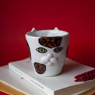 Handmade ceramic mug with a cat face design, available in calico, tuxedo, white, and orange cat variations. Perfect for cat lovers looking to add a cute, personalized touch to their drinkware collection.