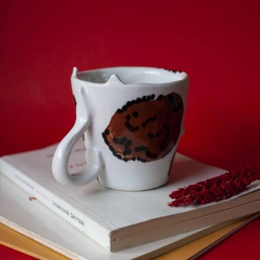 Handmade ceramic mug with a cat face design, available in calico, tuxedo, white, and orange cat variations. Perfect for cat lovers looking to add a cute, personalized touch to their drinkware collection.