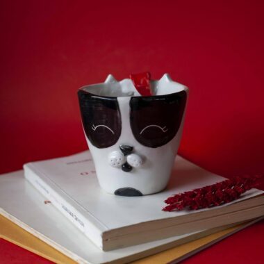 Handmade ceramic mug with a cat face design, available in calico, tuxedo, white, and orange cat variations. Perfect for cat lovers looking to add a cute, personalized touch to their drinkware collection.