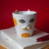 Handmade ceramic mug with a cat face design, available in calico, tuxedo, white, and orange cat variations. Perfect for cat lovers looking to add a cute, personalized touch to their drinkware collection." Greek: "Χειροποίητη κεραμική κούπα με σχέδιο προσώπου γάτας, διαθέσιμη σε εκδόσεις τρίχρωμης, δίχρωμης, λευκής και πορτοκαλί γάτας. Ιδανική για φιλόζωους που θέλουν να προσθέσουν μια χαριτωμένη, προσωπική πινελιά στη συλλογή τους από κούπες.