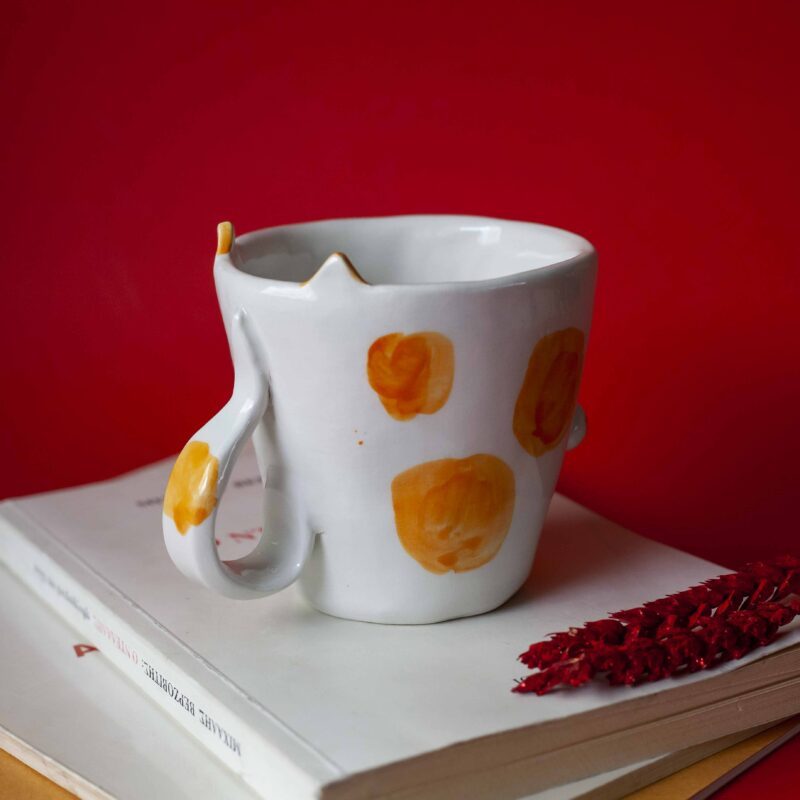 Handmade ceramic mug with a cat face design, available in calico, tuxedo, white, and orange cat variations. Perfect for cat lovers looking to add a cute, personalized touch to their drinkware collection." Greek: "Χειροποίητη κεραμική κούπα με σχέδιο προσώπου γάτας, διαθέσιμη σε εκδόσεις τρίχρωμης, δίχρωμης, λευκής και πορτοκαλί γάτας. Ιδανική για φιλόζωους που θέλουν να προσθέσουν μια χαριτωμένη, προσωπική πινελιά στη συλλογή τους από κούπες.