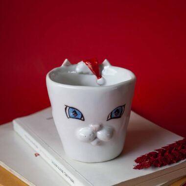 Handmade ceramic mug with a cat face design, available in calico, tuxedo, white, and orange cat variations. Perfect for cat lovers looking to add a cute, personalized touch to their drinkware collection.