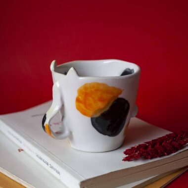 Handmade ceramic mug with a cat face design, available in calico, tuxedo, white, and orange cat variations. Perfect for cat lovers looking to add a cute, personalized touch to their drinkware collection.