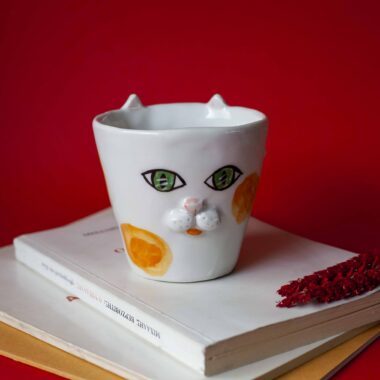 Handmade ceramic mug with a cat face design, available in calico, tuxedo, white, and orange cat variations. Perfect for cat lovers looking to add a cute, personalized touch to their drinkware collection.