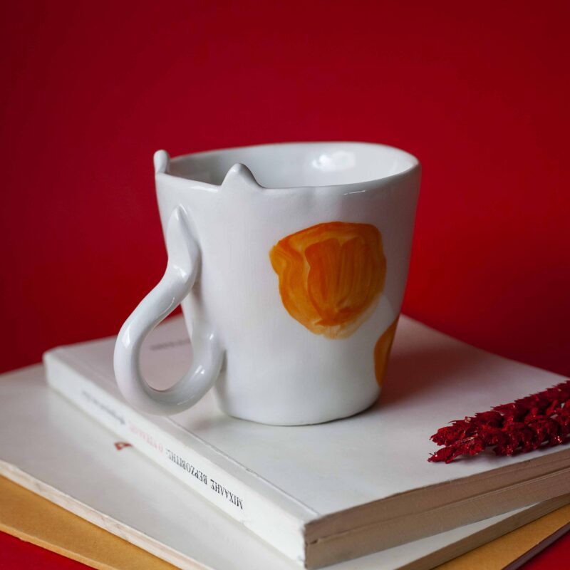 Handmade ceramic mug with a cat face design, available in calico, tuxedo, white, and orange cat variations. Perfect for cat lovers looking to add a cute, personalized touch to their drinkware collection." Greek: "Χειροποίητη κεραμική κούπα με σχέδιο προσώπου γάτας, διαθέσιμη σε εκδόσεις τρίχρωμης, δίχρωμης, λευκής και πορτοκαλί γάτας. Ιδανική για φιλόζωους που θέλουν να προσθέσουν μια χαριτωμένη, προσωπική πινελιά στη συλλογή τους από κούπες.