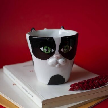 Handmade ceramic mug with a cat face design, available in calico, tuxedo, white, and orange cat variations. Perfect for cat lovers looking to add a cute, personalized touch to their drinkware collection.