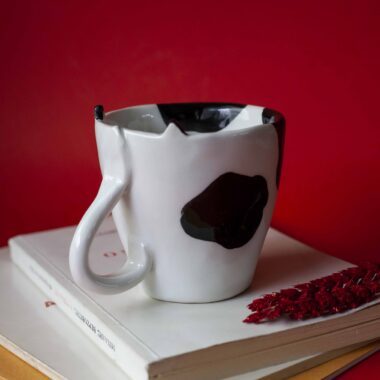 Handmade ceramic mug with a cat face design, available in calico, tuxedo, white, and orange cat variations. Perfect for cat lovers looking to add a cute, personalized touch to their drinkware collection.